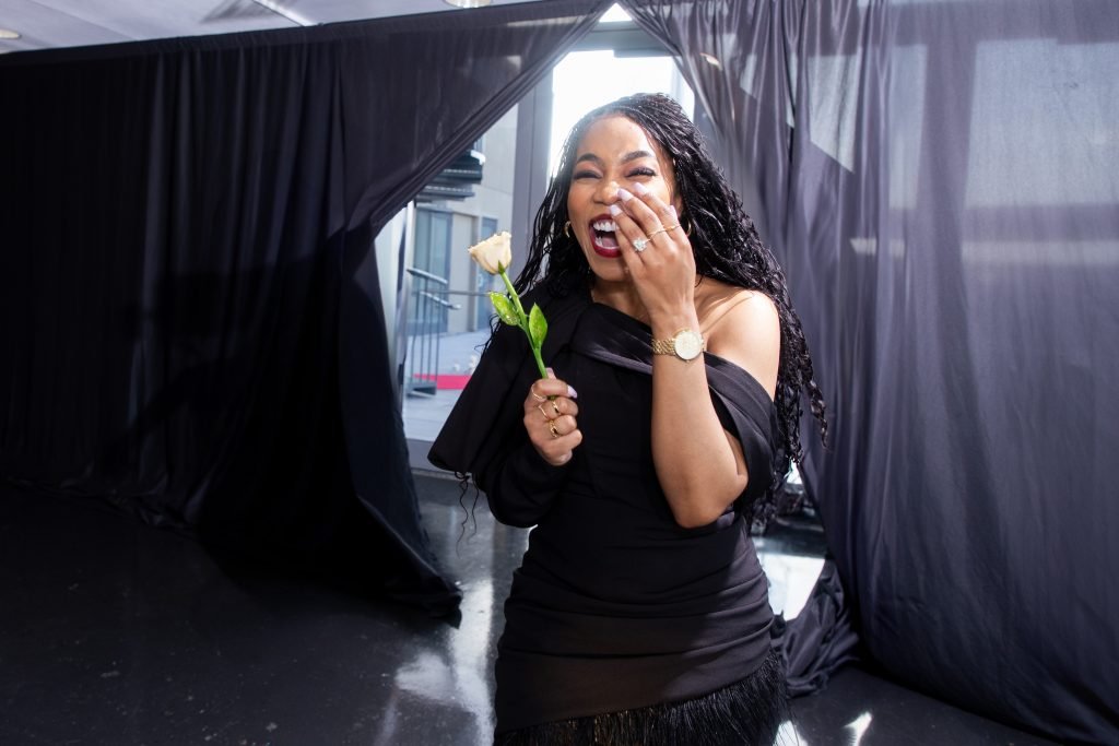 The bride-to-be holding a white rose and laughing with joyful tears as she walks through draped curtains into the surprise party.