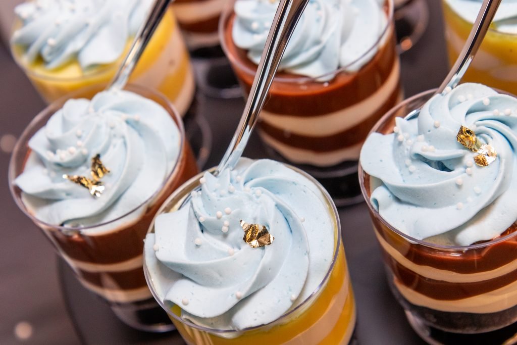 Artfully layered dessert shooters in individual cups, showing distinct layers of chocolate, vanilla, and light blue cream by JP Sweets.